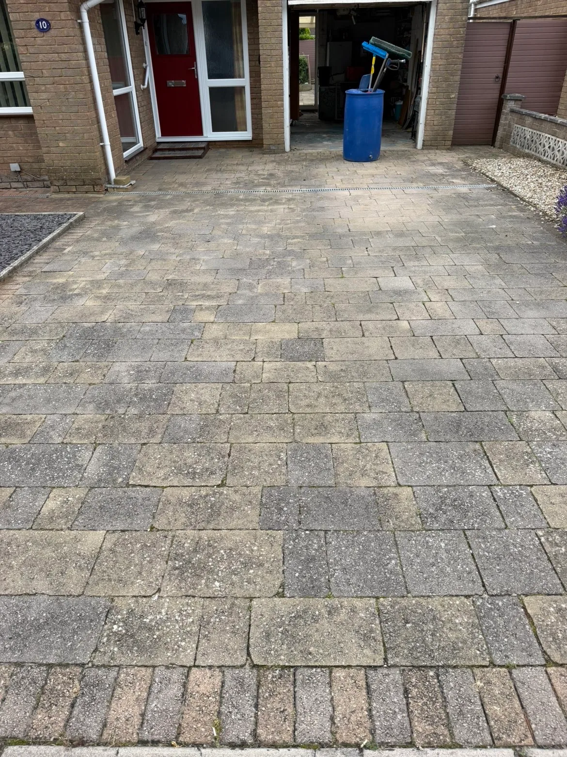 A block paved driveway part way through cleaning, the cleaned half clearly lighter than the rest